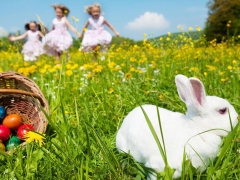 Mandje met beschilderde paaseieren en een wit konijn met spelende kinderen in een weiland